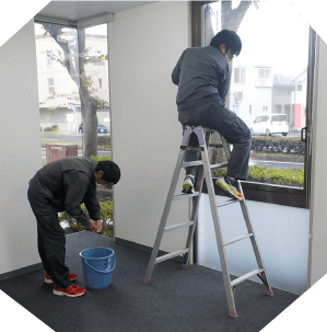 オフィス内で脚立を使い、窓ふきをしている場面